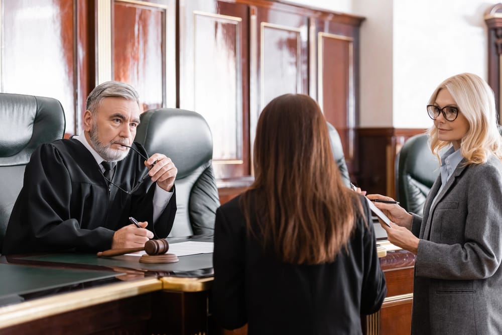 Fotografía sencilla de un mazo de juez sobre una mesa de madera, con documentos legales y un fondo desenfocado de una sala de tribunal.